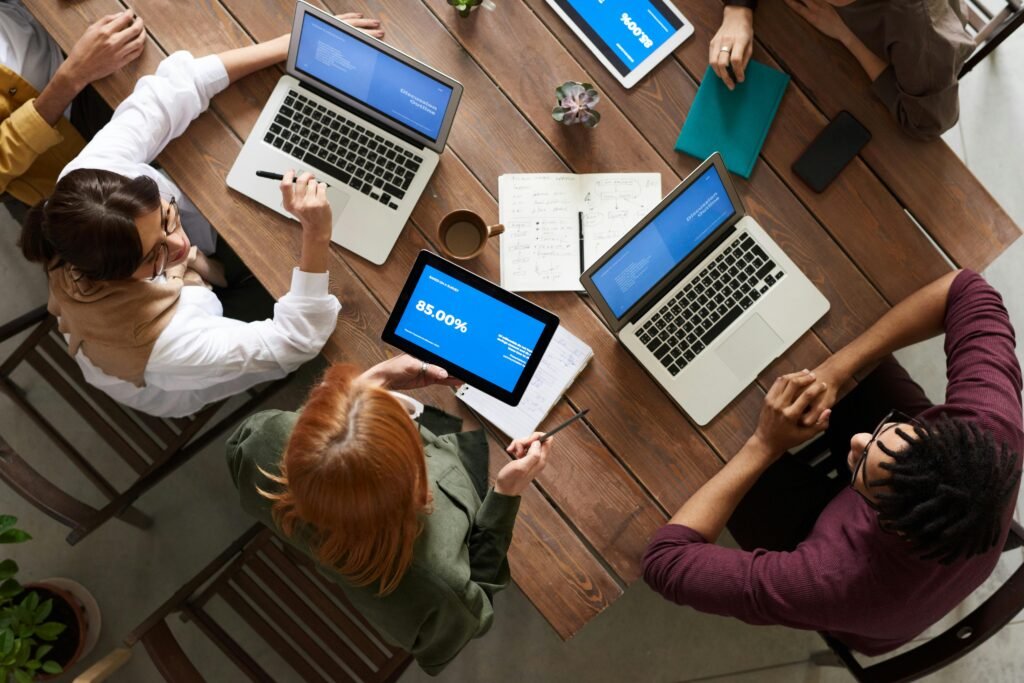 pexels-photo-3182773-3182773 Diverse team discussing business strategies with laptops and tablets at a wooden table.
